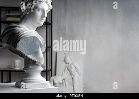 Gott Apoll Büste Skulptur. Antike griechische Gott der Sonne und der Poesie Gips Kopie einer Marmorstatue auf Grange Beton Wand Hintergrund im Studio. Copyspace Stockfoto