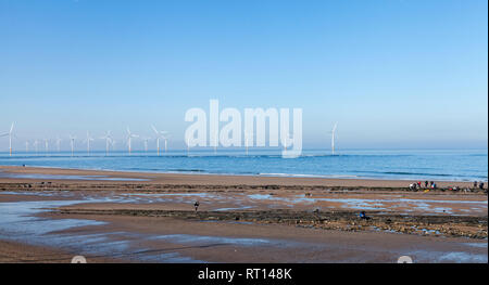 Einen sonnigen Tag an der Küste in Redcar, England, Großbritannien mit Studenten, Kurs arbeiten am Strand und Windenergieanlagen im Hintergrund Stockfoto