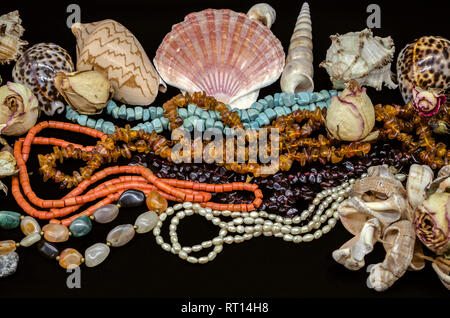 Schwarzer Hintergrund mit Muscheln und Perlen aus Türkis, rote Koralle, Bernstein, Granatapfel, bunte Achat, Perlen unter trockenen Knospen Stockfoto