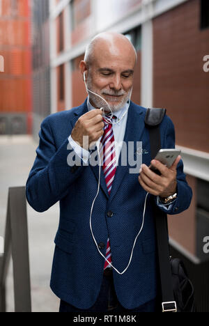 Senior Geschäftsmann mit Mobiltelefon- und Ohrhörer im Freien Stockfoto