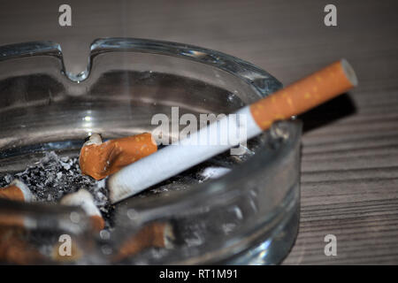 Brennende Zigarette in Glas Aschenbecher mit Zigarettenkippen Stockfoto