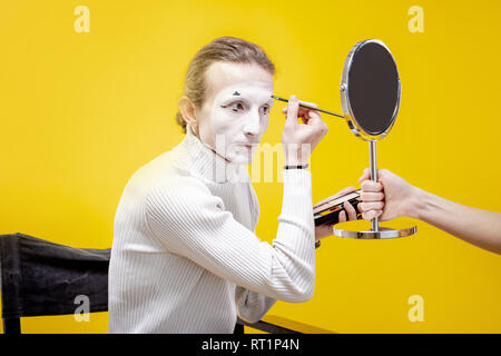 Schauspieler Anwendung gesichts Make-up für Pantomime performance sititng im Studio auf dem gelben Hintergrund Stockfoto