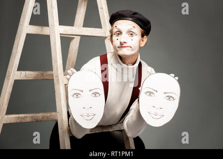 Porträt einer pantoomime Schauspieler holding Gesichtsmasken im Studio mit Leiter auf grauem Hintergrund Stockfoto