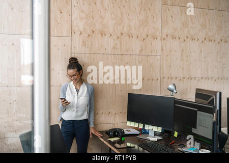 Junge Frau, die in Büros über smaftphone, Lachen Stockfoto