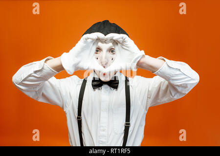 Porträt eines Schauspielers als Pantomime mit weißem Gesicht Make-up zeigt ausdrucksstarke Emotionen auf dem orangen Hintergrund im Studio Stockfoto