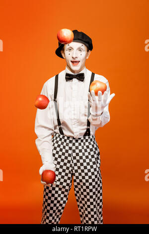 Porträt eines Schauspielers als Pantomime mit weißem Gesicht Make-up zeigt ausdrucksstarke Emotionen auf dem orangen Hintergrund im Studio Stockfoto