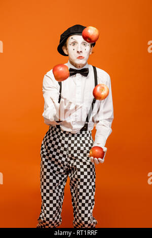 Porträt eines Schauspielers als Pantomime mit weißem Gesicht Make-up zeigt ausdrucksstarke Emotionen auf dem orangen Hintergrund im Studio Stockfoto