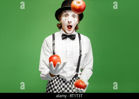 Pantomime mit weißem Gesicht Make-up Jonglieren mit Äpfel auf dem grünen Hintergrund im Studio Stockfoto