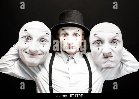 Porträt einer pantoomime hält zwei Gesichtsmasken mit unterschiedlichen Emotionen auf dem schwarzen Hintergrund. Konzept der Persönlichkeit split Stockfoto