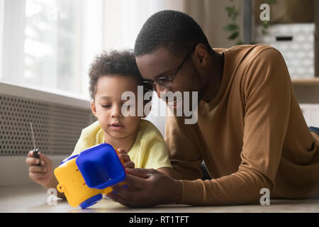 Kleiner Sohn holding Schraubendreher Instandsetzung Spielzeugauto spielen mit Papa Stockfoto