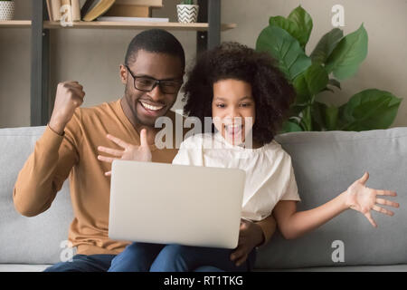 Aufgeregt afrikanischen Vater und Kind Mädchen Sieger am Laptop suchen Stockfoto