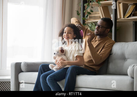 Afrikanische Vati bürsten Sie das Haar der Tochter sitzen auf einem Sofa Stockfoto
