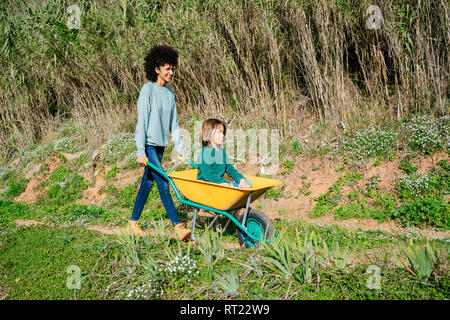 Vater gehen auf einem Feldweg, Schubkarre, mit seinem Sohn sitzen Stockfoto