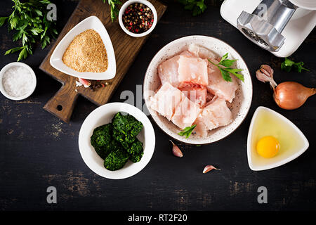 Zutaten für selbstgemachte Kuchen Kabeljau Fisch, Spinat, Ei und Semmelbrösel. Rohe Koteletts aus Hackfleisch/Cod. Ansicht von oben. Stockfoto