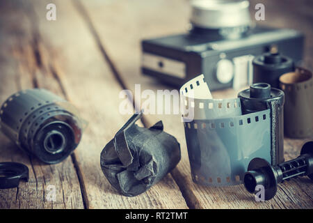 Altes Foto Filmrollen und Kassette auf alten hölzernen Schreibtisch, vintage Kamera im Hintergrund. Retro getönt. Stockfoto