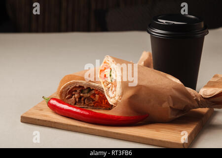 Kaffee und Shawarma chicken Roll in lavash mit frischem Gemüse und Sauce auf Holzbrett auf grauem Hintergrund. Stockfoto