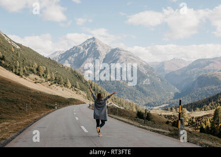 Schweiz, Engadin, Rückansicht der glückliche Frau mit erhobenen Armen auf Mountain Road Stockfoto
