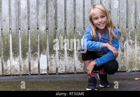 Portrait von lächelnden blonde Mädchen Hocken vor der hölzernen Wand Stockfoto