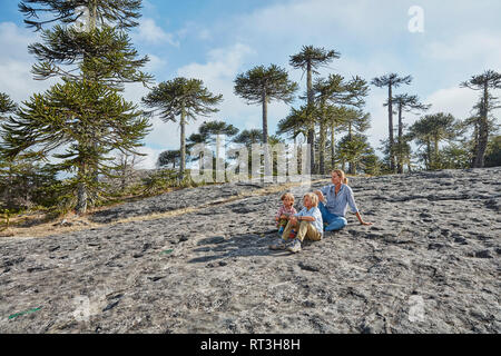 Chile, Puren, El Melado Nationalpark, Frau sitzt mit Söhnen auf Boulder in Araucaria forest Stockfoto