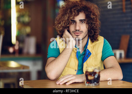 Porträt eines jungen Mannes mit Bart und lockiges Haar trinken Cola in einem Pub Stockfoto