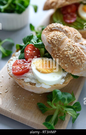 Bagel Sandwiches mit Frischkäse, Avocado, Tomate, Ei und Grüns auf grau Holz- Hintergrund. Selektive konzentrieren. Gesunde Ernährung oder vegetarisches Essen co Stockfoto