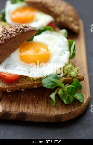 Roggen Sandwiches (Burger) mit Avocado, Tomaten, Spiegelei und Grüns auf braunem Holz- Hintergrund. Selektive konzentrieren. Gesunde Ernährung oder vegetarisches Essen con Stockfoto