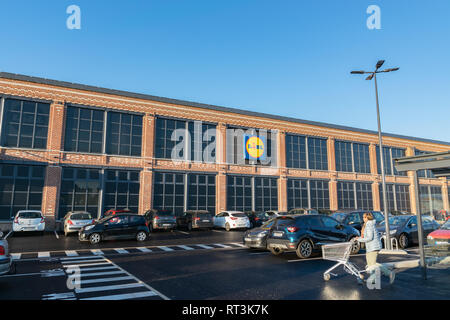 Tourcoing, Frankreich - Februar 27,2019: Gebäude, Logo, Autos auf dem Parkplatz und eine Frau mit einem Warenkorb mit dem Lidl Supermarkt gehen. Stockfoto