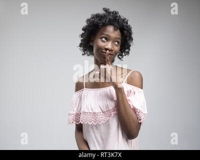 Geheimnis, Klatsch-Konzept. Junge Frau ruft zur Ruhe. Frau am trendigen Grauen studio Hintergrund isoliert. Junge emotionale afrikanische Frau. Menschliche Gefühle, Mimik Konzept. Stockfoto