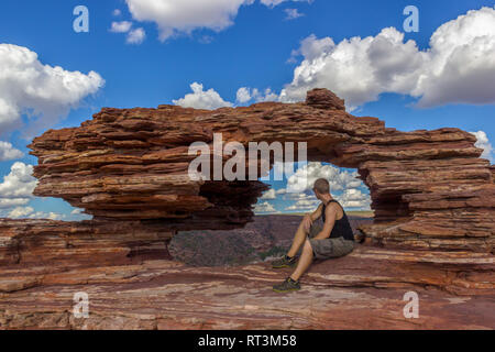 Junger Mann in der Natur, eine natürliche Arch Rock Formation in Kalbarri National Park an einem sonnigen Tag sitzen, Western Australia Stockfoto