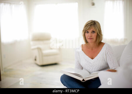 Porträt einer Mitte der erwachsenen Frau mit einem Buch auf der Couch in Ihrem Hause zu sitzen. Stockfoto