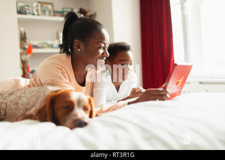 Mutter und Sohn mit digitalen Tablet auf dem Bett neben schlafenden Hund Stockfoto