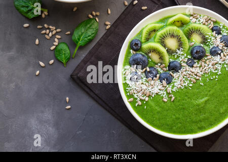 Frühstück grünen Smoothie Schüssel mit Kiwi, Blaubeeren und Sonnenblumenkerne auf grauem Beton Hintergrund. Ansicht von oben. Stockfoto