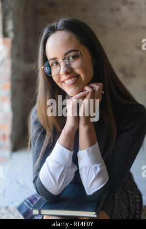 Portrait von Schulmädchen Brille in die Kamera schaut beim Sitzen auf der Treppe Stockfoto