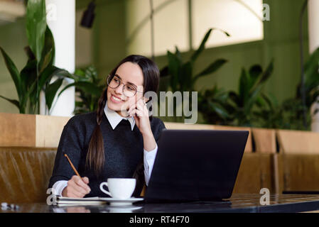 Univercity brunette Mädchen mit Zöpfen die Vorbereitung auf die Prüfung mit Laptop, während als das Trinken von Kaffee in einem Cafe Stockfoto