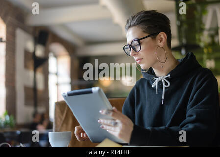 Verträumt attraktive Verknüpfung Student in Elegante optische Brillen an den hölzernen Tisch in der Cafeteria bei einer Tasse Kaffee und Tablet Stockfoto