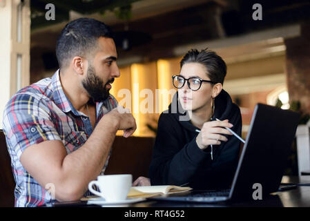 Zwei geschickte Mitschüler mit freundlichen Gespräch beim Hausaufgaben machen, die sie mit dem Laptop im Cafe innen Stockfoto