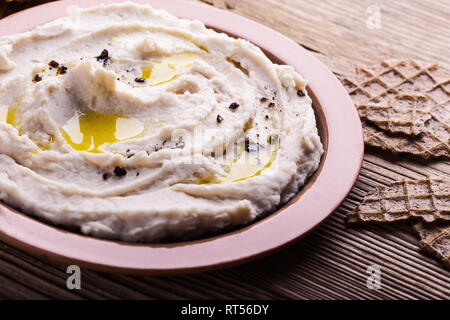 Weiße Bohnen hummus serviert mit Roggen Waffeln auf Holztisch, gesunden Snack dip, Nahaufnahme, selektiver Fokus Stockfoto