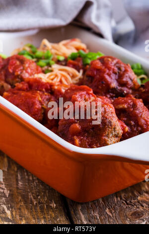 Hausgemachtes Rindfleisch Frikadellen mit Spaghetti in marinara Sauce Auflaufform auf rustikalen Holztisch serviert traditionelle italienische Küche, Nahaufnahme, selec Stockfoto