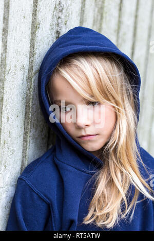 Portrait von traurigen blonde Mädchen trägt blaue Kapuzenjacke gegen Holz Wand lehnt Stockfoto