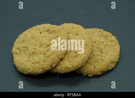 Drei Haferflocken Kekse auf einem schwarzen schiefergedeckt Platte krümelig und bereit zu essen. Stockfoto