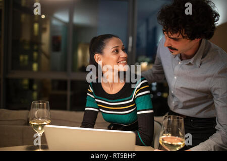 Paar mit Laptop und trinken Wein zu Hause in der Nacht Stockfoto