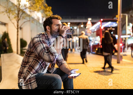 UK, London, Mann sitzt auf einer Bank in der Nacht das Trinken aus Becher Stockfoto