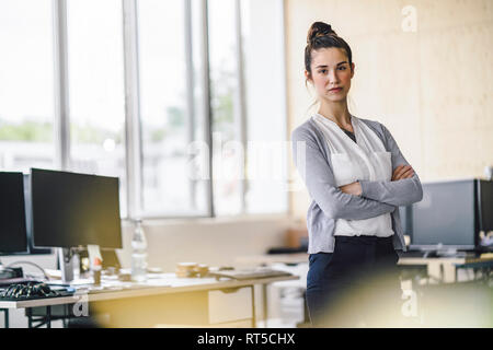 Porträt einer schönen jungen Frau, stehend im Büro, mit verschränkten Armen Stockfoto