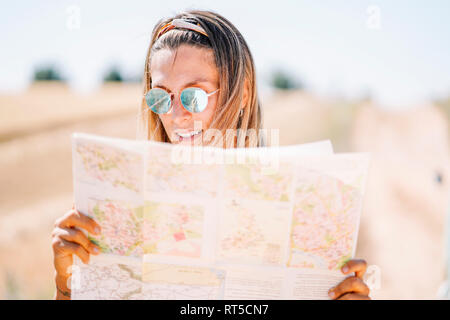 Blonde junge Frau mit verspiegelten Sonnenbrillen Orientieren mit Karte Stockfoto