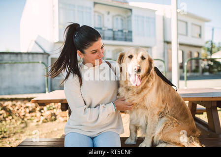 Lächelnde junge Frau mit ihrem Golden Retriever Hund ruht im Freien Stockfoto