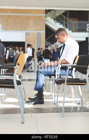 Geschäftsmann sitzt auf einem Stuhl und mit Laptop in einem Warteraum Stockfoto