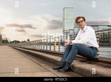 Deutschland, Berlin, Porträt der Geschäftsmann mit Smartphone Entspannen an der Spree Stockfoto