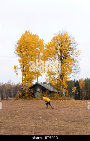 Finnland, Kuopio, Frau in gelb Regenjacke sammeln Blätter im Herbst Stockfoto
