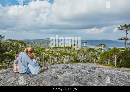 Chile, Puren, El Melado Nationalpark, Frau sitzt mit Söhnen auf Boulder bei Araucaria Forest suchen Stockfoto