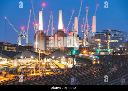 Vereinigtes Königreich, England, London, Ansicht von Gleisen und Zügen am Abend, ehemaliger Battersea Power Station und Krane im Hintergrund Stockfoto